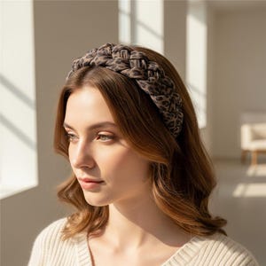 May include: A braided headband with a leopard print pattern in shades of brown and black. The headband is worn on the head. The background is a neutral color.