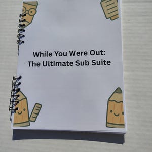 May include: A spiral-bound notepad with a white cover featuring the text "While You Were Out: The Ultimate Sub Suite." The cover is decorated with cartoon pencils in yellow and brown. The notepad is on a light gray surface.