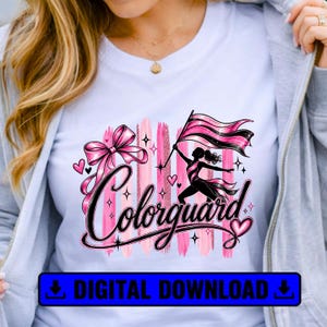 May include: A white t-shirt featuring a graphic design with the word Colorguard in black script. The design includes a pink bow, a silhouette of a person holding a flag, pink brushstroke accents, small hearts, and star shapes throughout.