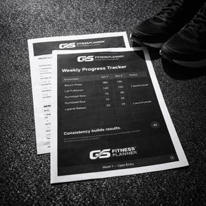 May include: A monochrome image featuring a fitness planner with the text "Weekly Progress Tracker" and exercise details. The planner is on a textured surface with black athletic shoes in the background. The planner includes the text "Consistency builds results."