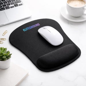 Könnte beinhalten: Schwarzes ergonomisches Mauspads mit integrierter Handgelenkauflage und dem Wort ELITEGROUND in Farbverlauf. Eine weiße kabellose Maus liegt auf dem Pad. Eine Tasse Kaffee, eine Sukkulente und ein Laptop sind ebenfalls im Bild.