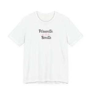Puede incluir: Una camiseta blanca de manga corta con el texto negro Peruanita Bonita impreso en el pecho. Entre las dos palabras hay tres pequeños corazones rojos dibujados con líneas finas, conectados por una línea horizontal continua centrada.