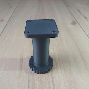 Peut inclure: Un pied de meuble noir mat doté d'une plaque de montage supérieure carrée avec quatre trous de vis pré-percés, d'une colonne centrale cylindrique et d'une base circulaire avec un bord dentelé en forme d'engrenage pour le réglage.