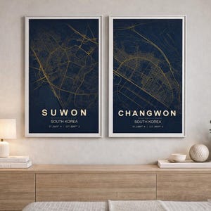 Op de afbeelding: Twee ingelijste stadsplattegronden. De kaarten tonen goudkleurige straatindelingen op een donkerblauwe achtergrond. De print links zegt "SUWON SOUTH KOREA" en de print rechts "CHANGWON SOUTH KOREA".