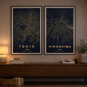 Puede incluir: Dos impresiones enmarcadas de mapas de ciudades japonesas. Los mapas de Tokio e Hiroshima son dorados sobre un fondo azul oscuro. Los nombres de las ciudades son dorados, con el nombre del país debajo. Las impresiones se exhiben sobre un mueble de madera.