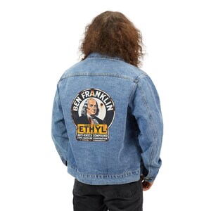 May include: A light blue denim jacket with a large circular graphic on the back. The graphic features an image of Benjamin Franklin, the word "ETHYL", and the text "ANTI-KNOCK COMPOUND ETHYL GASOLINE CORPORATION".