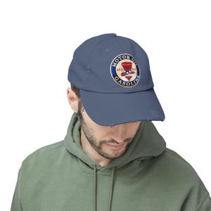 May include: A faded blue baseball cap with a circular emblem reading "MOTOR OIL RED HAT GASOLINE." The emblem features a red top hat and stars. The cap has a pre-curved peak and a distressed look.