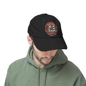 May include: Black distressed baseball cap with a circular graphic. The graphic features the text "ORION AERO SPARK PLUGS" and a vintage airplane illustration in red, white, and blue. The cap has a curved brim and a distressed, worn appearance.