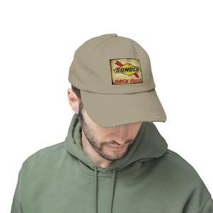 May include: A tan baseball cap with a distressed brim. The cap features a rectangular patch with the text "SUNOCO RACE FUELS" in red and yellow. The cap is made of a soft material.