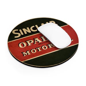 May include: A round mousepad with a vintage design featuring the words "SINCLAIR OPAL MOTOR" in gold lettering on a red and black background. A white wireless mouse rests on the pad.