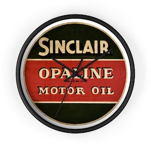 Puede incluir: Reloj de pared redondo con marco negro. La esfera del reloj presenta un diseño vintage de Sinclair Opaline Motor Oil en rojo, verde y beige. Las manecillas del reloj son negras.