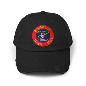 May include: Black distressed baseball cap with a vintage Oldsmobile Rocket 8 logo. The logo is circular with red, blue, and yellow accents, and includes the text "OLDSMOBILE SERVICE + SALES" and "Rocket 8".
