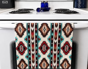 Op de afbeelding: Een decoratieve keukendoek met een geometrisch patroon uit het zuidwesten. De doek heeft een crèmekleurige achtergrond met herhaalde ruit- en zigzagontwerpen in bruin, rood en turquoise. Het hangt aan een witte oven.
