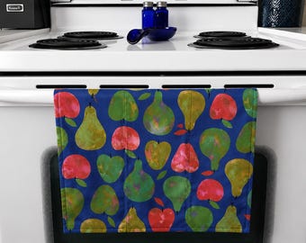 Op de afbeelding: Een blauwe keukendoek met een herhaald patroon van aquarelperen en appelvormen in groen, rood en geel. De handdoek hangt aan een ovenhandvat.
