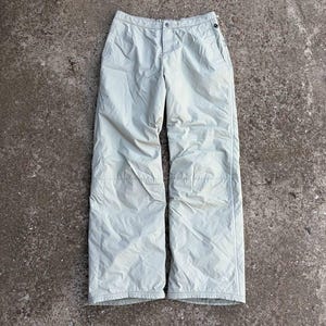 Puede incluir: Pantalones de nieve verde claro con cierre de botón y cremallera. Los pantalones tienen un diseño de pierna recta con una raya blanca en el lateral y un pequeño logotipo cerca del dobladillo. Fabricados con material ligero.