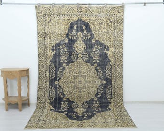 May include: A large rectangular area rug featuring a dark navy blue central medallion and field surrounded by a wide beige border. The rug displays intricate floral and vine patterns throughout, with a distressed texture and a fringed bottom edge.