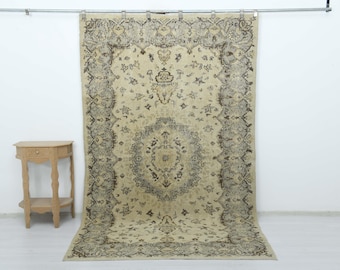 Puede incluir: Una alfombra rectangular grande con base beige y patrones intrincados de flores y enredaderas en marrón oscuro. El diseño incluye un medallón central rodeado por un borde detallado. Una pequeña mesa auxiliar de madera clara con un cajón está al lado.
