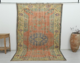Puede incluir: Una alfombra rectangular grande que presenta un medallón central azul sobre un campo naranja vibrante, rodeado por un borde ancho de color crema con intrincados patrones geométricos y florales en tonos azul, verde y morado.