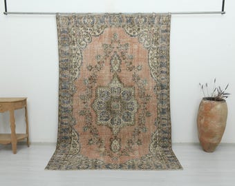 Puede incluir: Una alfombra rectangular grande con un centro de color melocotón descolorido y un medallón floral central en azul y crema. La alfombra está enmarcada por un borde ancho e intrincado en tonos azul, crema y melocotón con motivos florales.