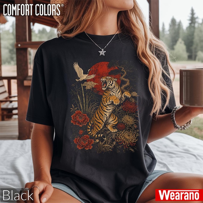 May include: A black short-sleeve t-shirt featuring a graphic print of a roaring tiger, a flying crane, red flowers, and a large red sun. The design includes bamboo stalks and yellow chrysanthemums. The shirt has a crew neckline and a relaxed fit.