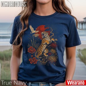 May include: A navy blue t-shirt featuring a graphic print of a roaring tiger, a flying crane, red flowers, and a large red sun. The text COMFORT COLORS is printed in the top left corner, and the text True Navy is at the bottom left.