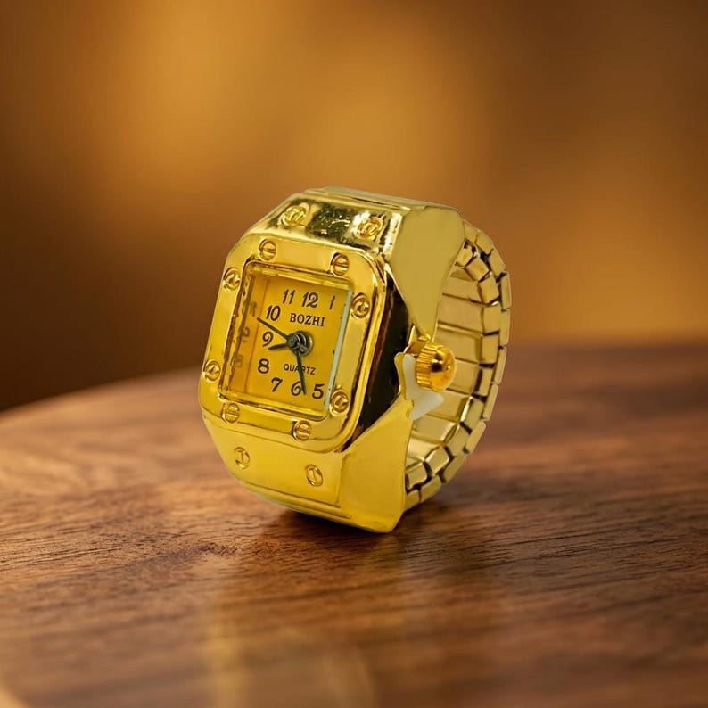 May include: A gold-colored ring watch with a square face and a gold band. The watch face is yellow with black numerals and hands. The watch is marked "BOZHI" and "QUARTZ".