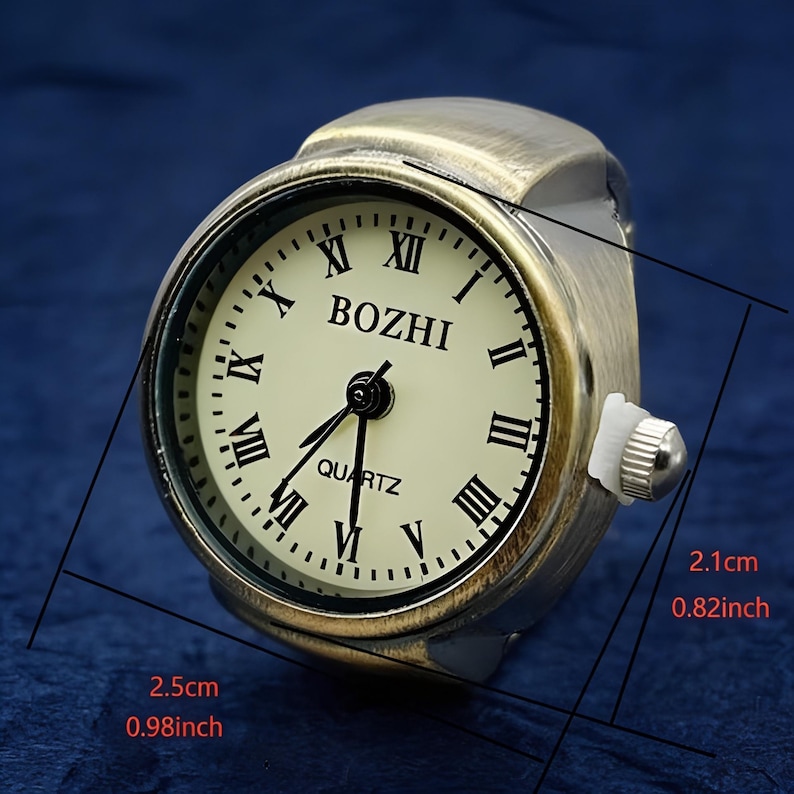 May include: Antique-style ring watch with a cream-colored face and black Roman numerals. The watch face is marked "BOZHI" and "QUARTZ". The ring watch measures 0.98 inches wide and 0.82 inches high.