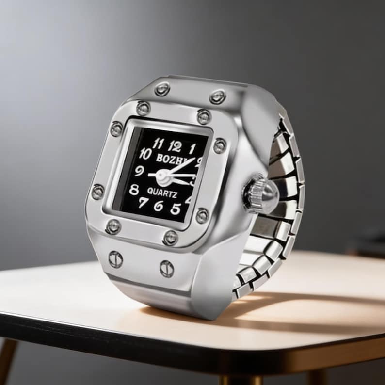 May include: A silver-toned ring watch with a square black face displaying white numerals and hands. The watch band is a flexible, linked design. The watch face is marked with the word "BOZHY" and "QUARTZ".