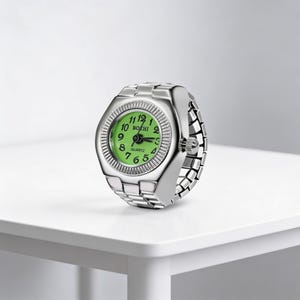 May include: A silver ring watch with a green face and quartz movement. The watch face is round with black numerals and hands. The band is made of linked metal. The watch is displayed on a white surface.