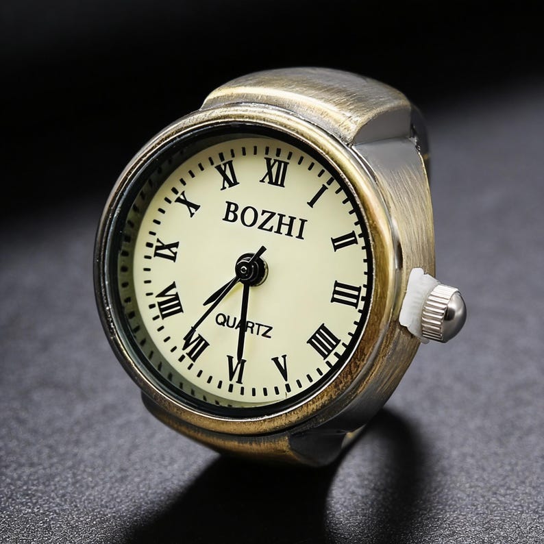 May include: A vintage-style ring watch with a cream-colored face and black Roman numerals. The watch face displays the brand name "BOZHI" and "QUARTZ". The ring is made of a bronze-colored metal.