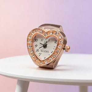 May include: A rose gold heart-shaped ring watch with a white face and crystal accents. The watch face displays the time with black numerals and hands. The brand name "BOZHI" is printed on the watch face.