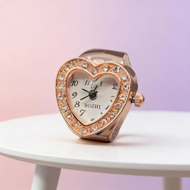 May include: A rose gold heart-shaped ring watch with a white face and crystal accents. The watch face displays the time with black numerals and hands. The brand name "BOZHI" is printed on the watch face.