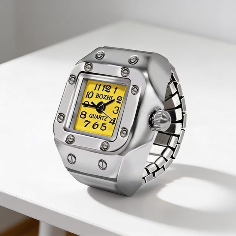 May include: Silver ring watch with a square yellow face. The watch has black numerals and hands, with the word "BOZHI" above the centre. The ring band is a flexible, linked design. A unique accessory.