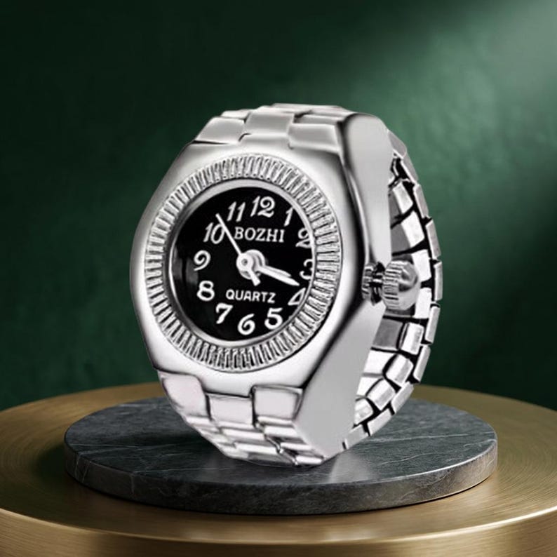 May include: A silver ring watch with a black face and white numerals. The watch face displays the brand name "BOZHI" and the word "QUARTZ". The band is made of interlocking metal links.