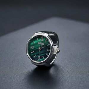 May include: A silver ring watch with a green face. The watch face has Roman numerals and the brand name "BOZH". The ring watch is set against a dark background.