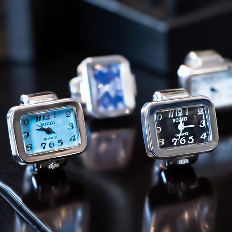 May include: Close-up of several silver quartz ring watches with rectangular faces. One watch has a light blue face with black numerals and hands, while another has a black face with white numerals. The brand name "BOZHI" is visible.