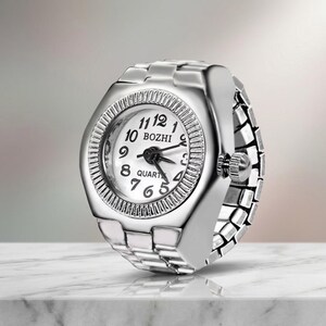 May include: A silver ring watch with a white face and black hands. The watch face displays the numbers 1 to 12 and the word "BOZHI". The ring band is made of linked metal pieces.