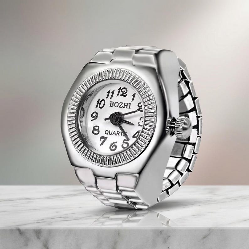May include: A silver ring watch with a white face and black hands. The watch face displays the numbers 1 to 12 and the word "BOZHI". The ring band is made of linked metal pieces.