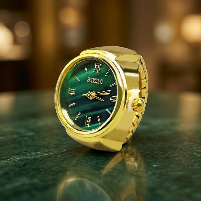 May include: A gold-toned ring watch with a green face and Roman numerals. The watch face has the brand name "BOZHI" printed on it. The band is made of gold-colored metal links.
