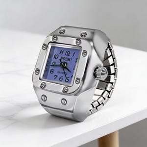 May include: A silver-toned ring watch with a square face and a blue dial. The watch features a quartz movement and the brand name "BOZHI". The band is made of linked metal pieces, and the watch is set on a white surface.