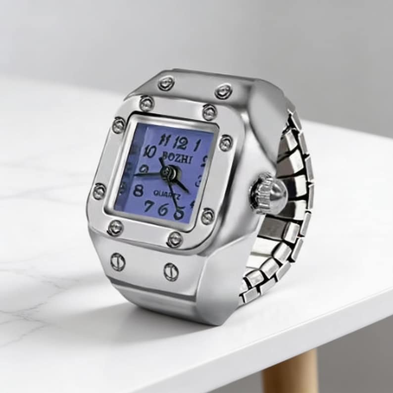 May include: A silver-toned ring watch with a square face and a blue dial. The watch features a quartz movement and the brand name "BOZHI". The band is made of linked metal pieces, and the watch is set on a white surface.