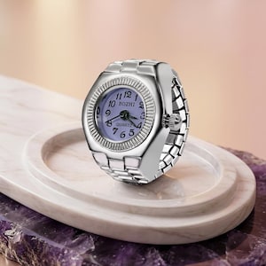 May include: A silver ring watch with a pale purple face and the word "BOZHI" printed on the watch face. The watch has a quartz movement and a flexible band. The watch is displayed on a white marble tray.