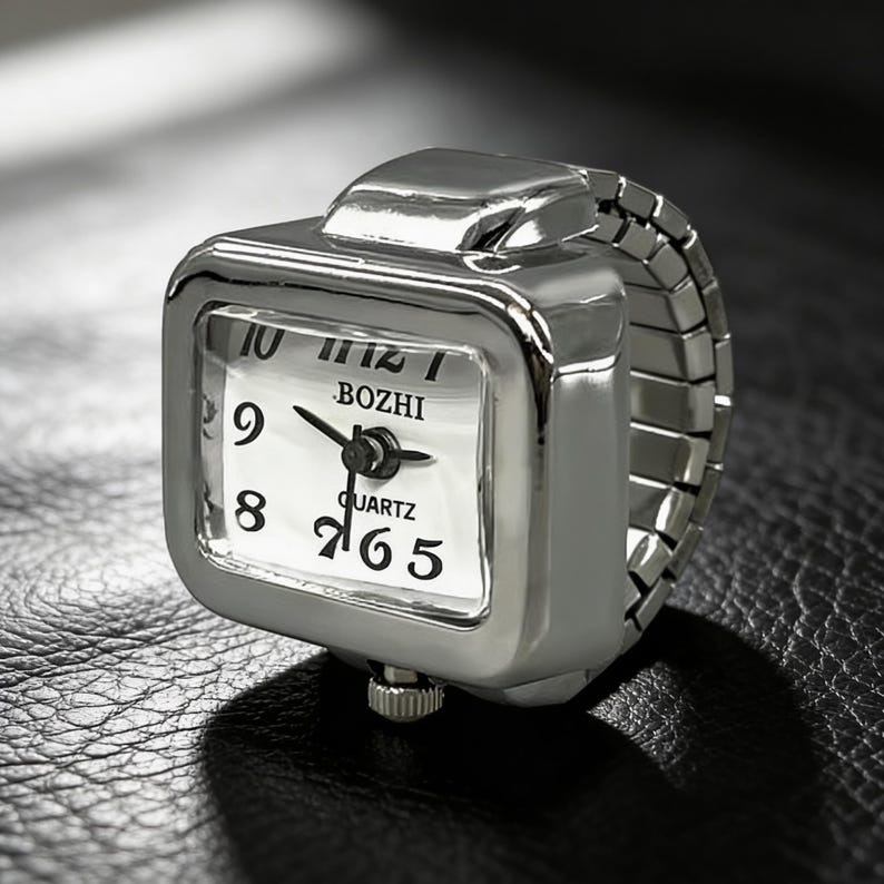 May include: A silver-toned ring watch with a square face and an elastic band. The watch face is white with black numerals and hands, and the brand name "BOZHI" is visible. The watch is a unique accessory.