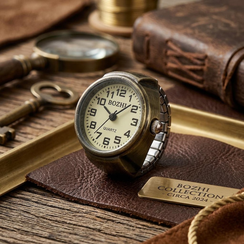 May include: A vintage-style ring watch with a cream-colored face and black numerals. The watch has a bronze-colored casing and a stretch band. The watch face reads "BOZHI COLLECTION - CIRCA 2024-". The watch is displayed on a leather surface.