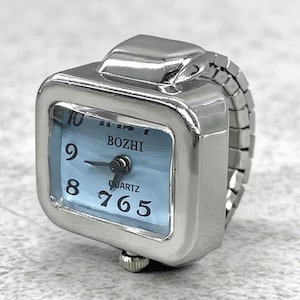 May include: A silver-toned ring watch with a square face and a light blue dial. The watch face displays the time with black numerals and hands. The band is made of linked metal. The word "BOZHI" is printed on the watch face.
