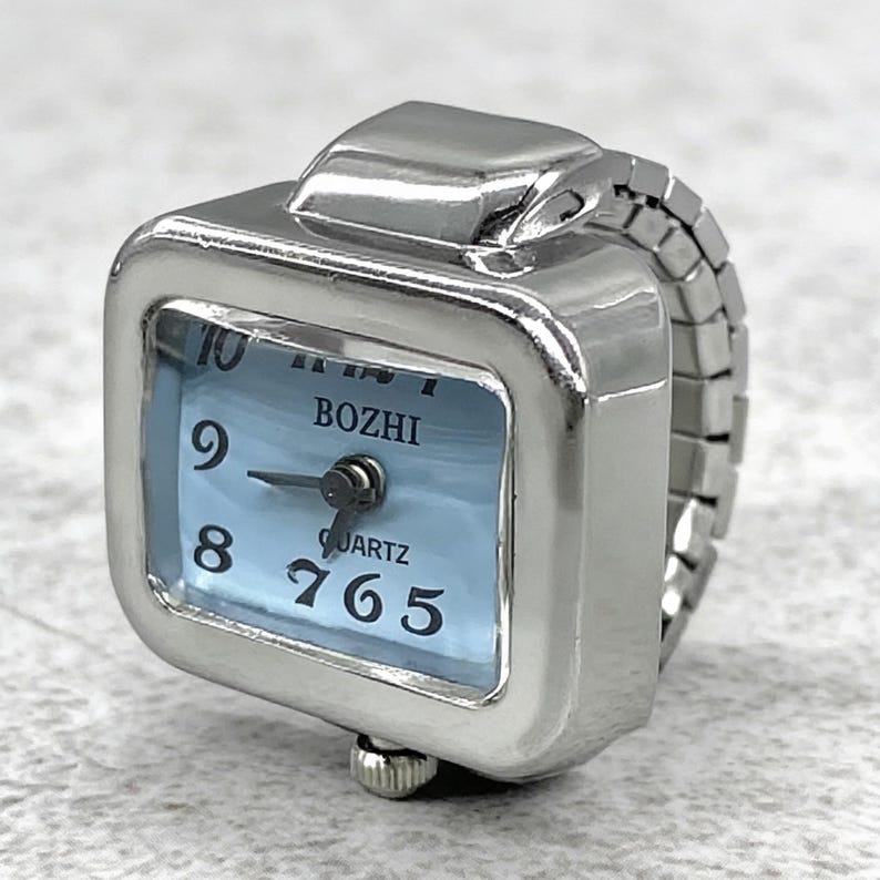 May include: A silver-toned ring watch with a square face and a light blue dial. The watch face displays the time with black numerals and hands. The band is made of linked metal. The word "BOZHI" is printed on the watch face.