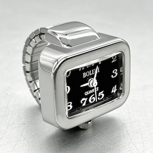 May include: A silver-toned ring watch with a rectangular face and a black dial. The watch face displays white numerals and hands, with the brand name "BOLEVI" visible. The band is a flexible, expandable design.