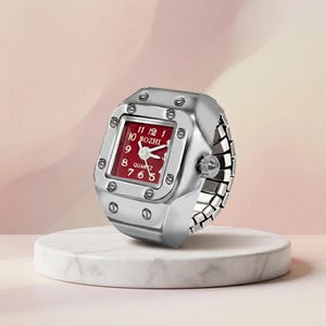 May include: A silver ring watch with a red face and white numerals. The watch face is square with the brand name "BOZHI" and the word "QUARTZ" visible. The watch is on a white marble stand.