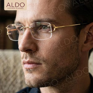 May include: Rimless eyeglasses with gold-colored metal frames. The glasses have a rectangular shape and are designed with a minimalist aesthetic. The brand name "ALDO VINTAGE GLASSES" is visible in the upper left corner.