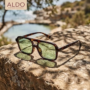 May include: Aviator-style sunglasses with a tortoiseshell frame and light green tinted lenses. The frame features a double bridge design. The text ALDO VINTAGE GLASSES is visible in the upper left corner of the image, presented in a tan box.